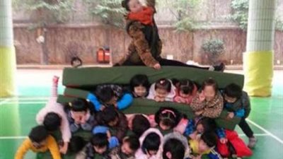 معلمة تجلس فوق عشرين طفلا اعمارهم من 4 الي 5 سنوات